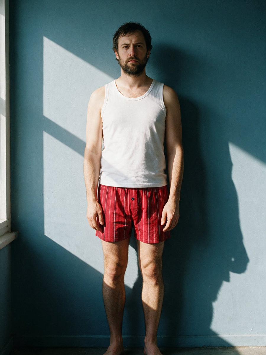 Man in red striped boxers and a white tank against a blue wall