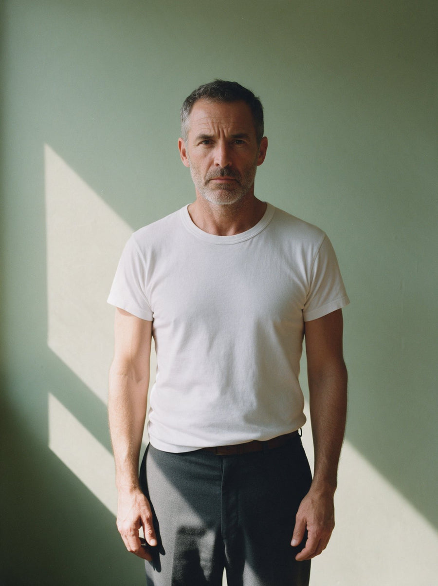 Man in a white crew neck undershirt against a sage green wall