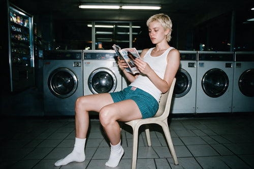 Woman reading a magazine in a laundromat at night
