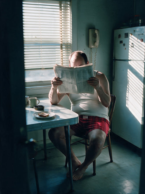 Man in striped boxers behind a newspaper at a kitchen table